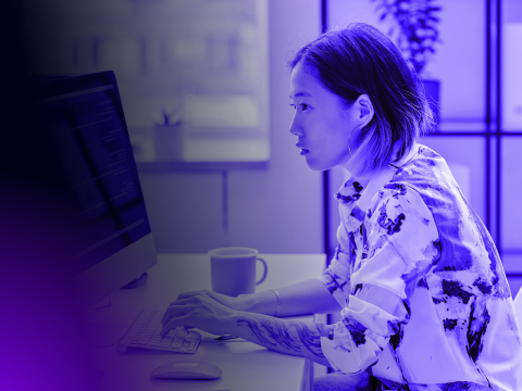 Woman sat at a desk in the office, writing code on her computer